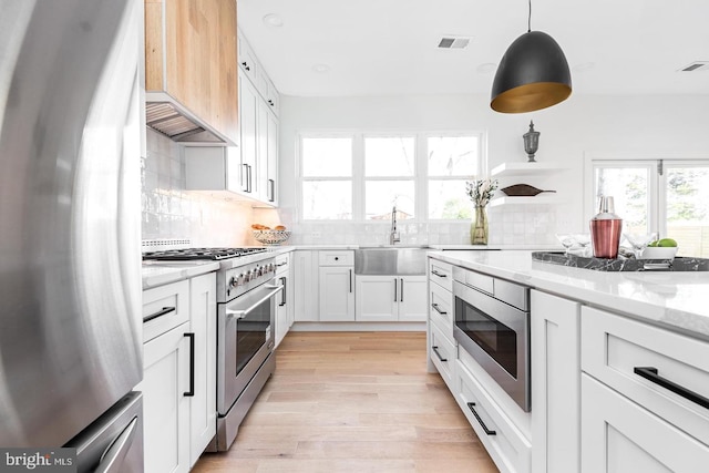 kitchen with visible vents, custom range hood, light stone counters, stainless steel appliances, and a sink