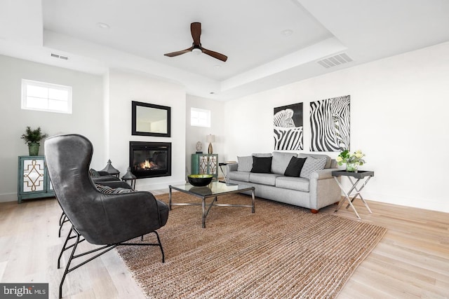 living room featuring visible vents, a raised ceiling, baseboards, and light wood-style flooring