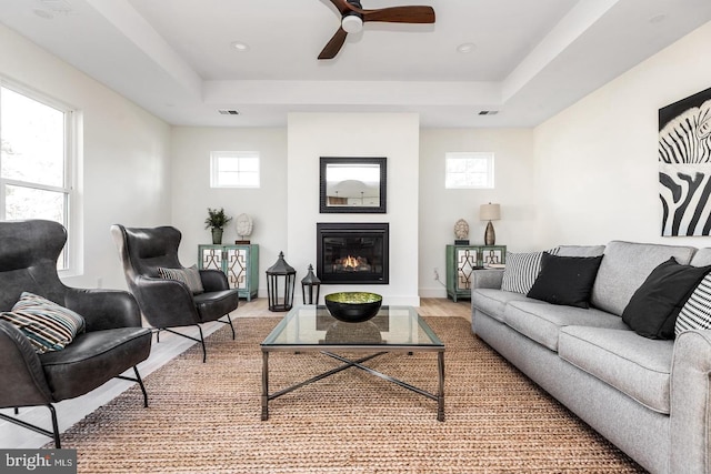 living room featuring a glass covered fireplace, a tray ceiling, baseboards, and wood finished floors