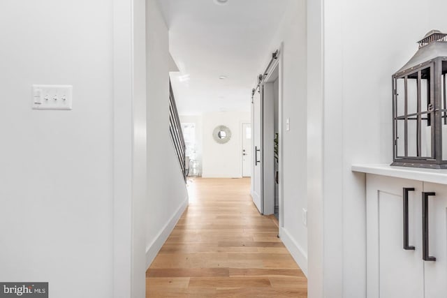 hall featuring a barn door, stairway, light wood-style floors, and baseboards