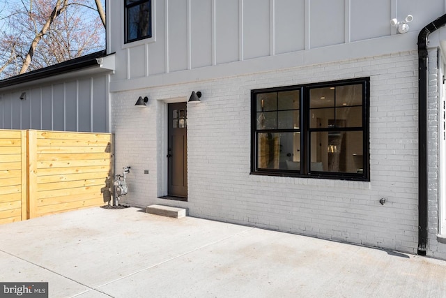 property entrance featuring a patio, fence, brick siding, and board and batten siding