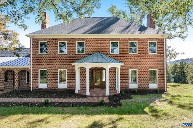 view of front of home featuring a standing seam roof, a front yard, and a chimney