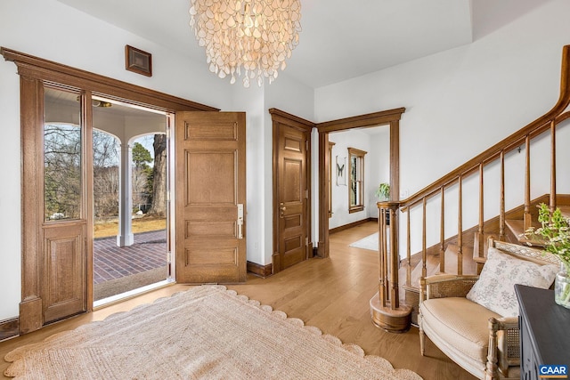 foyer featuring a chandelier, baseboards, light wood-style flooring, and stairs