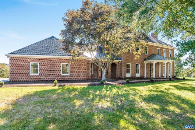 view of front facade with a front yard, brick siding, and roof with shingles