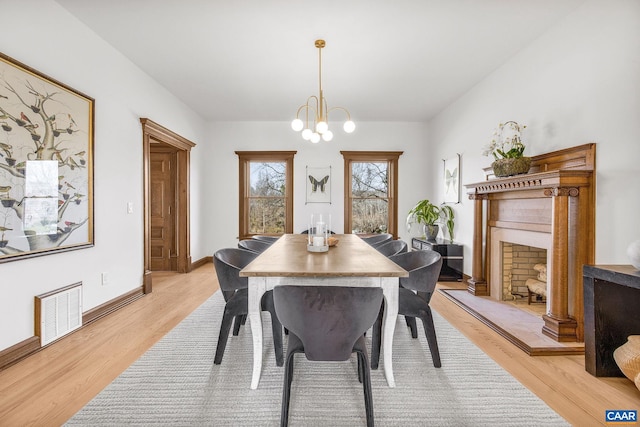 dining space featuring baseboards, visible vents, an inviting chandelier, a fireplace with raised hearth, and light wood-type flooring