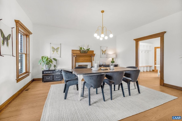 dining area featuring light wood-style flooring, a fireplace, baseboards, and a chandelier