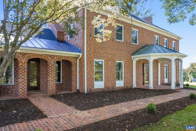 back of house with metal roof, brick siding, and a standing seam roof