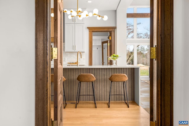 bar featuring tasteful backsplash, pendant lighting, light wood-type flooring, an inviting chandelier, and a sink