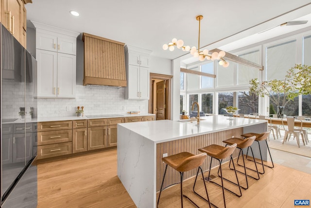 kitchen featuring tasteful backsplash, a breakfast bar area, light wood-style floors, custom exhaust hood, and a sink