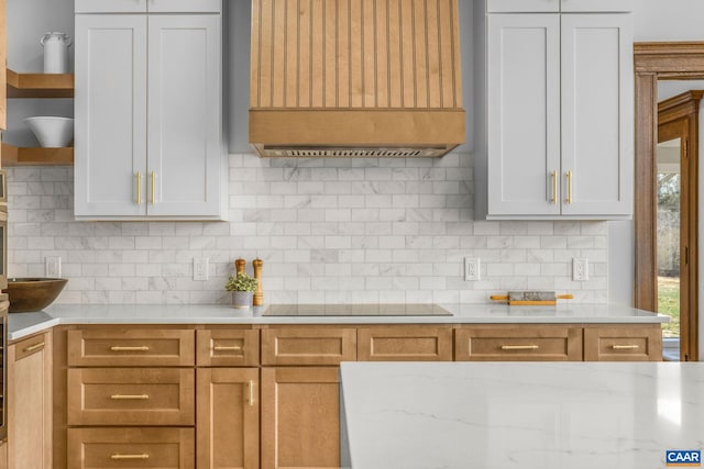 kitchen with light stone countertops, premium range hood, decorative backsplash, plenty of natural light, and black electric cooktop