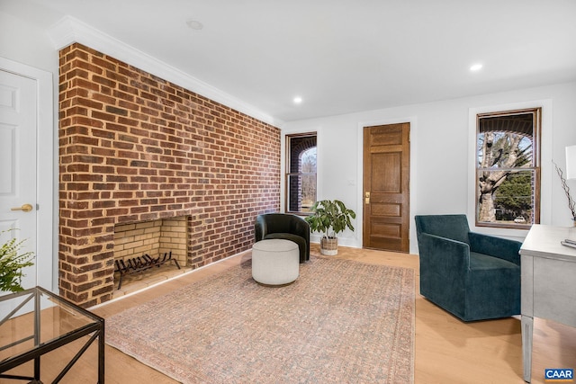 sitting room with crown molding, brick wall, a fireplace, and light wood finished floors