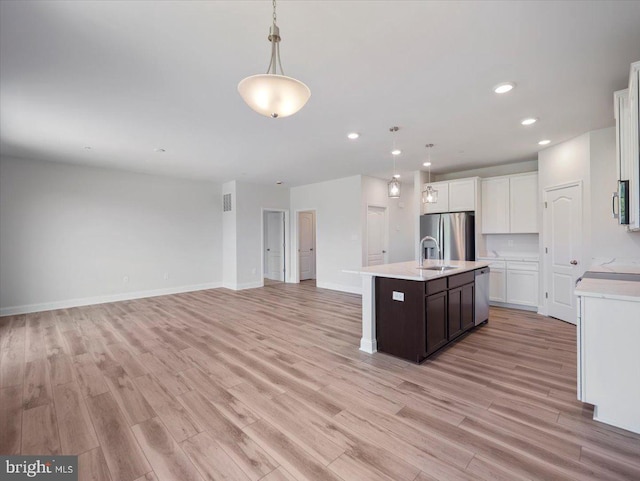 kitchen with open floor plan, light wood-style floors, appliances with stainless steel finishes, light countertops, and hanging light fixtures