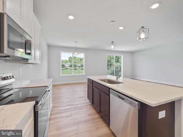 kitchen with light wood-type flooring, pendant lighting, a center island with sink, a sink, and stainless steel appliances