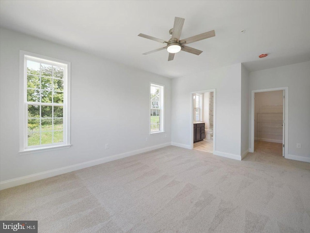 unfurnished bedroom featuring light colored carpet, ensuite bathroom, a walk in closet, and baseboards