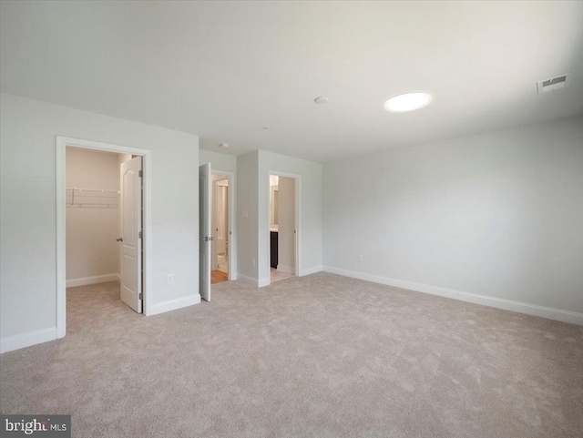 unfurnished bedroom with a walk in closet, light carpet, and baseboards