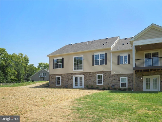 back of property with a balcony, a yard, french doors, and stone siding