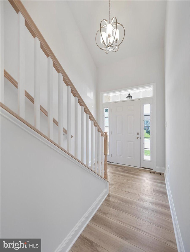 entrance foyer with light wood finished floors, a chandelier, a high ceiling, and baseboards