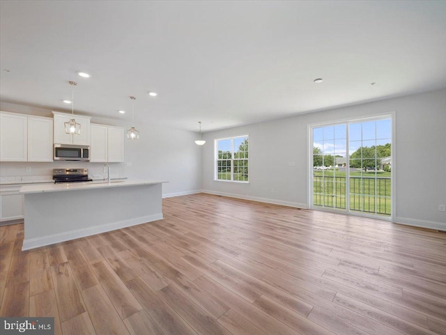 unfurnished living room featuring recessed lighting, light wood-type flooring, baseboards, and a sink