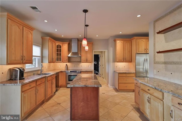 kitchen with a center island, wall chimney range hood, light stone countertops, stainless steel appliances, and a sink