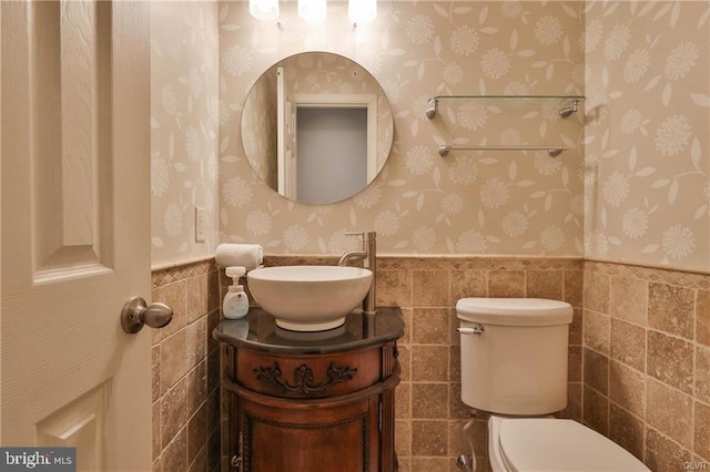 bathroom featuring toilet, tile walls, wainscoting, and wallpapered walls