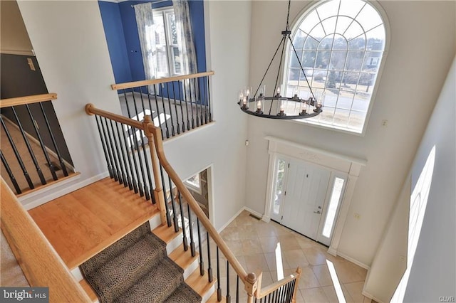 tiled entryway with baseboards, a notable chandelier, and a high ceiling