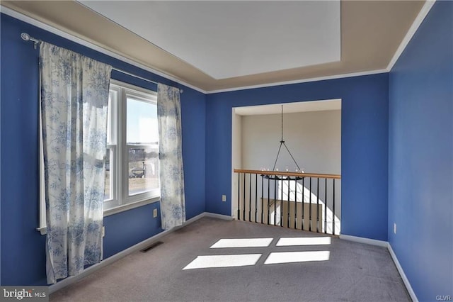 carpeted spare room featuring visible vents, a raised ceiling, crown molding, and baseboards