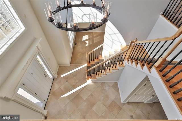 entryway with tile patterned floors, a notable chandelier, a towering ceiling, and stairs