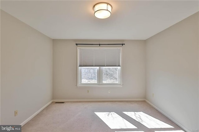 spare room featuring light colored carpet, visible vents, and baseboards