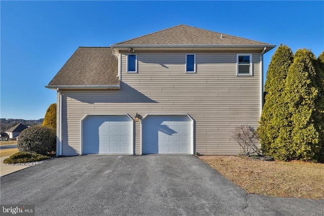 view of property exterior with a garage, roof with shingles, and driveway