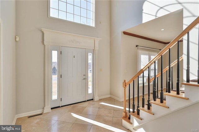 tiled entrance foyer with stairs, a high ceiling, visible vents, and baseboards