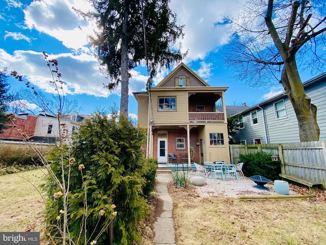 rear view of house with brick siding, a patio, a balcony, and fence