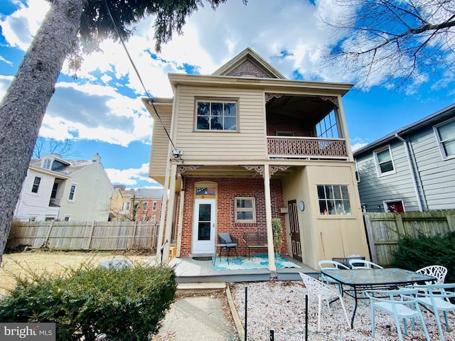 rear view of property featuring brick siding, outdoor dining area, a balcony, and fence