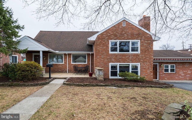 view of front of home with a front yard, brick siding, roof with shingles, and a chimney