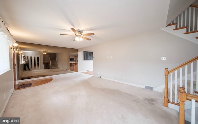 unfurnished living room with visible vents, carpet flooring, baseboards, ceiling fan, and stairs