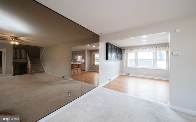 unfurnished living room with carpet, a ceiling fan, baseboards, recessed lighting, and stairs