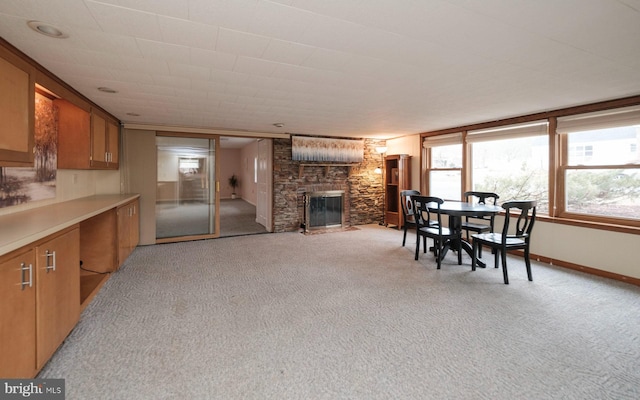 dining room featuring a stone fireplace, light colored carpet, and baseboards