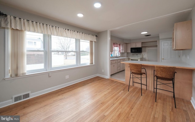 kitchen featuring visible vents, black microwave, light wood-style flooring, a peninsula, and white electric stove