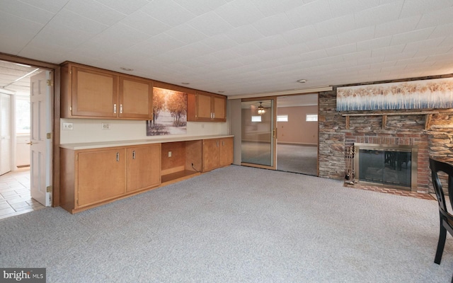 kitchen with light carpet, brown cabinetry, light countertops, and a large fireplace