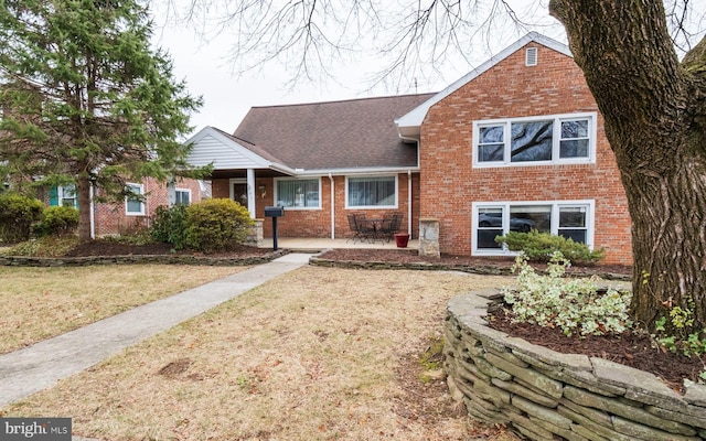 view of front of house with brick siding, a front yard, and a shingled roof