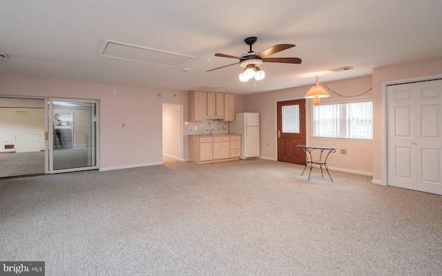 unfurnished living room with baseboards, visible vents, attic access, ceiling fan, and light colored carpet