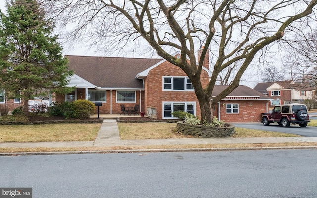 tri-level home with brick siding, a front yard, and roof with shingles