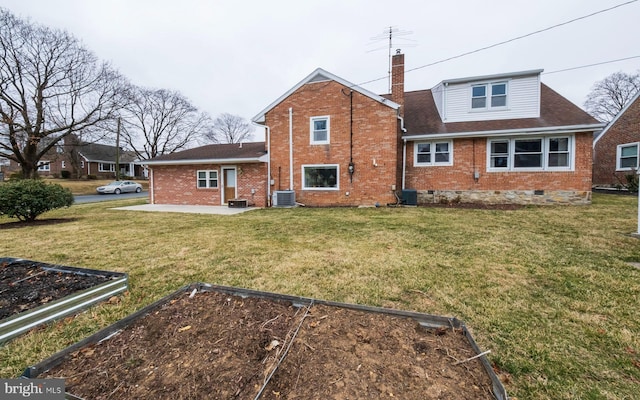 back of house with a garden, crawl space, brick siding, and a lawn