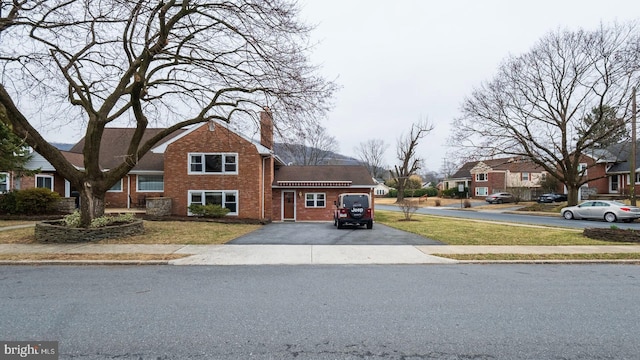 traditional-style home featuring a front yard, a residential view, brick siding, and driveway