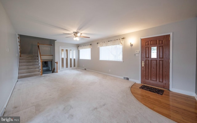 unfurnished living room featuring wood finished floors, baseboards, visible vents, ceiling fan, and stairs