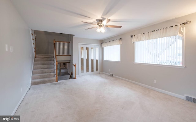 unfurnished living room with visible vents, baseboards, stairs, carpet floors, and a ceiling fan