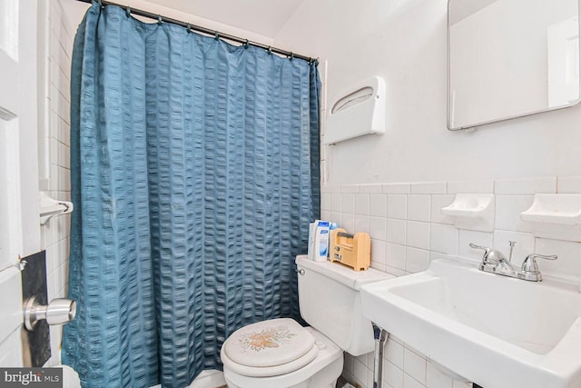 bathroom with a shower with shower curtain, a wainscoted wall, a sink, tile walls, and toilet