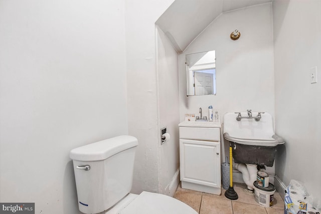 half bath with tile patterned floors, toilet, vanity, and vaulted ceiling