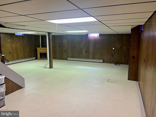 finished below grade area featuring a paneled ceiling, wood walls, and baseboard heating