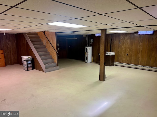 finished basement featuring stairway, wooden walls, baseboard heating, and water heater