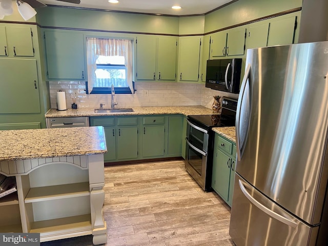 kitchen featuring light stone counters, light wood-style flooring, a sink, appliances with stainless steel finishes, and tasteful backsplash